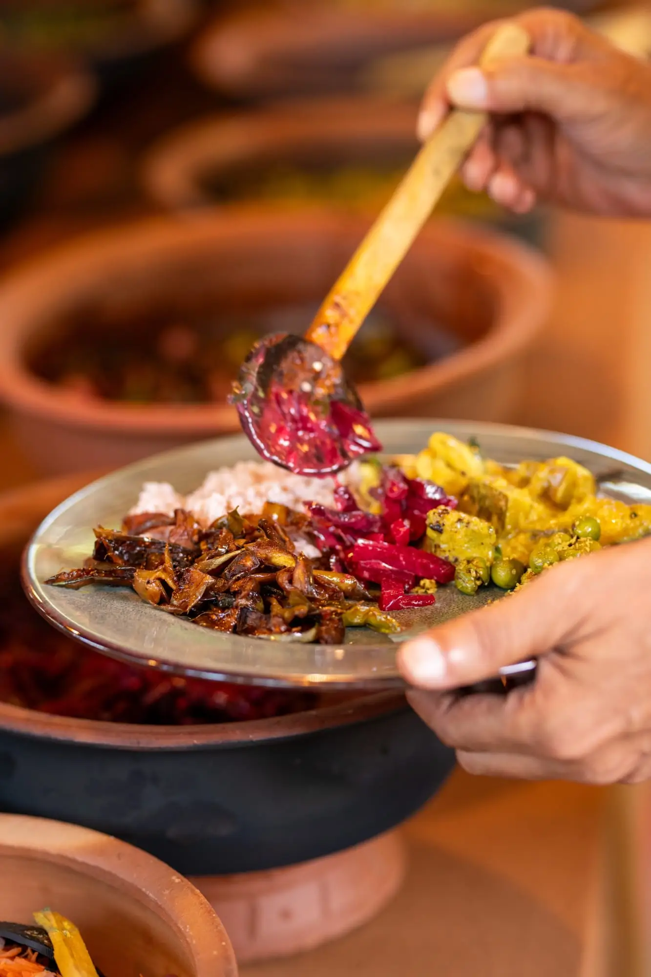 A plate being filled with rice and curries from the clay pots