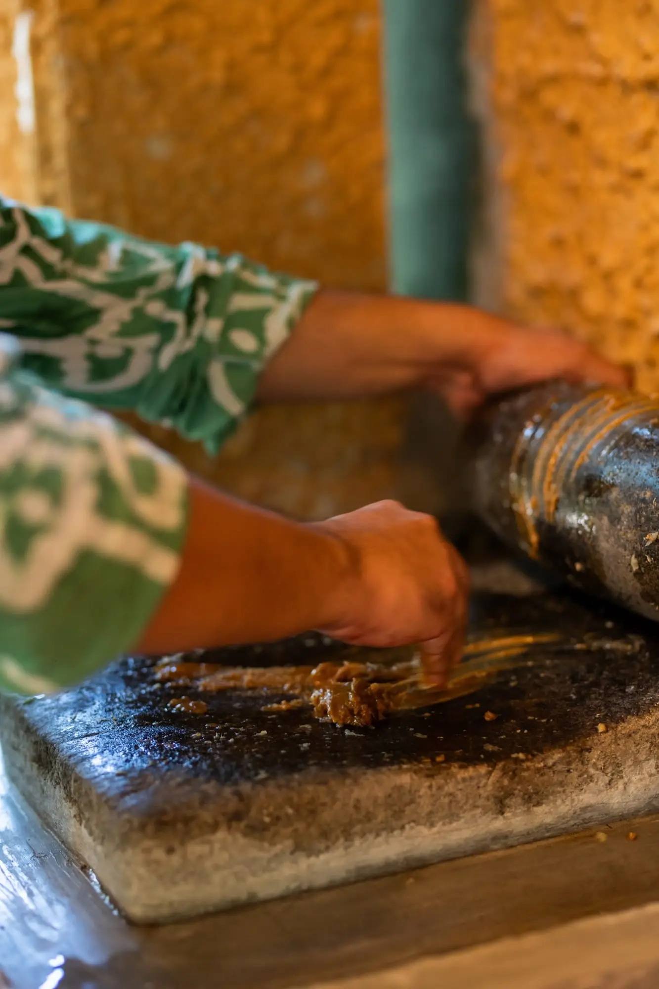 Hands grinding spices with a stone roller on a grinding stone